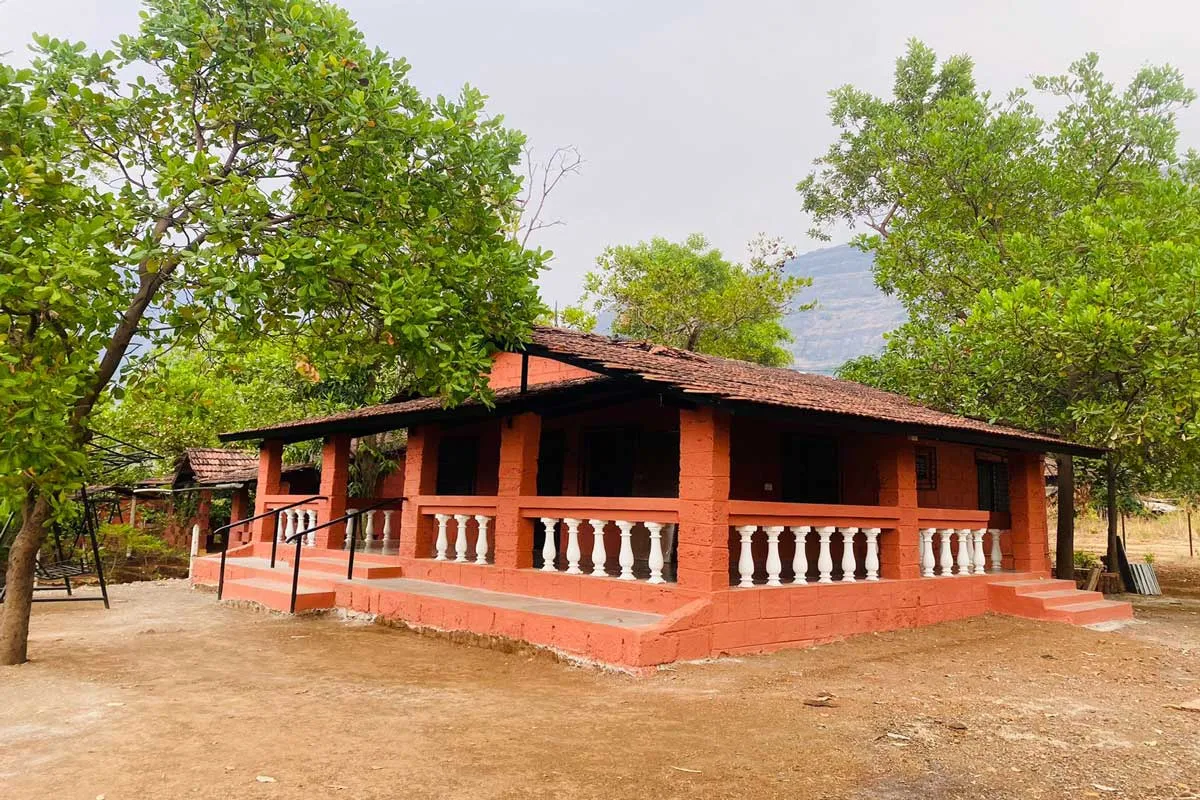 A single-story rustic guesthouse with a red-brown exterior, a white balustraded verandah, and a mountain view.